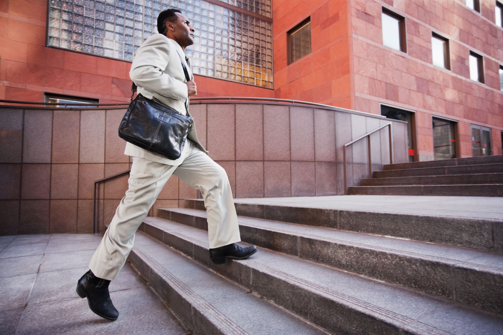 Businessman with satchel hurrying up steps in front of office building