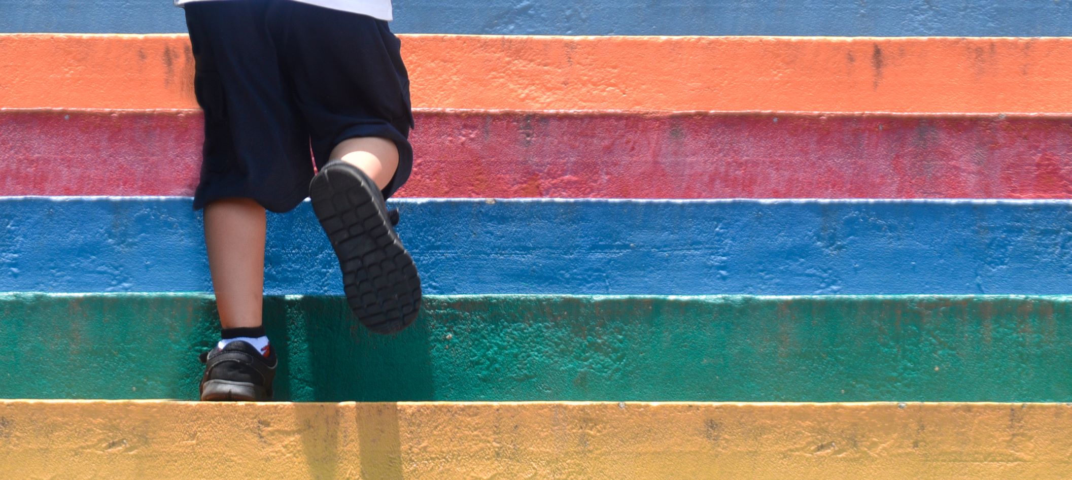 close-up of rainbow-colored steps, toddler's legs climbing up