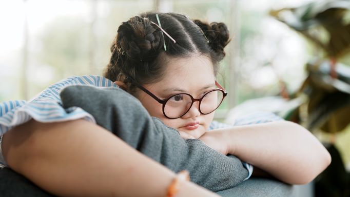 girl with Down Syndrome, wearing glasses, feeling sad or bored laying over back of couch